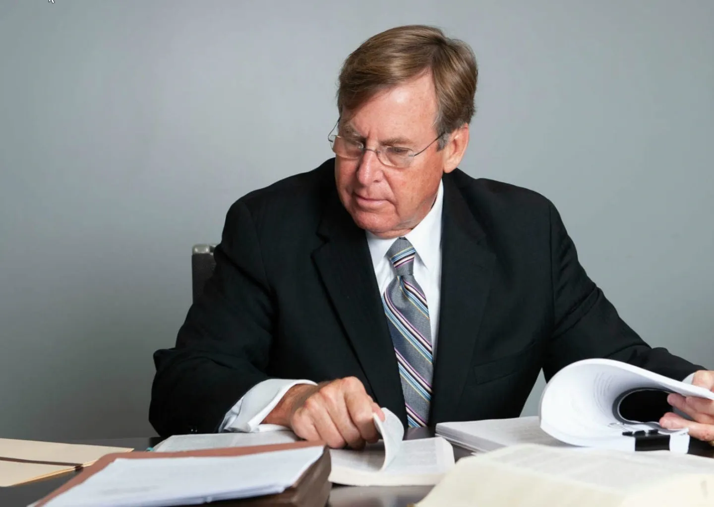 A man in suit and tie at desk with papers.